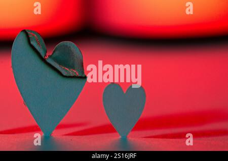 Two paper hearts on a red and pink background with shadows. One heart has been burnt and still has the ash. Stock Photo