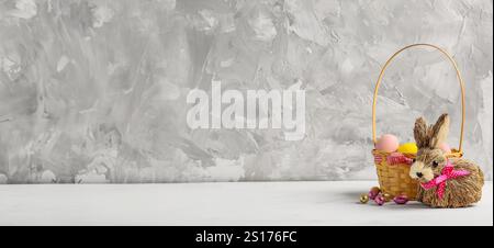 Toy Easter bunny and basket with painted eggs on grey grunge background with space for space Stock Photo
