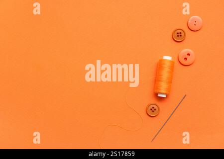 Thread spool, needle and buttons on orange background Stock Photo