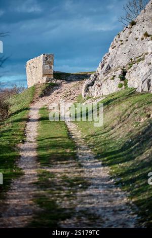 An image of a dirt path leading uphill towards an old stone structure, surrounded by rocky terrain and patches of greenery. Vitoriano, Araba, Basque C Stock Photo