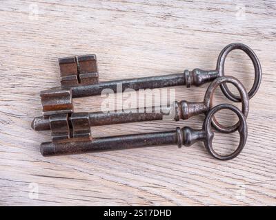 Three vintage iron keys on a wooden background. View from above. Stock Photo