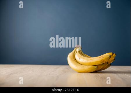 Fresh bunch of ripe, yellow bananas on a wooden surface, set against a soft blue background. With copy space. Stock Photo