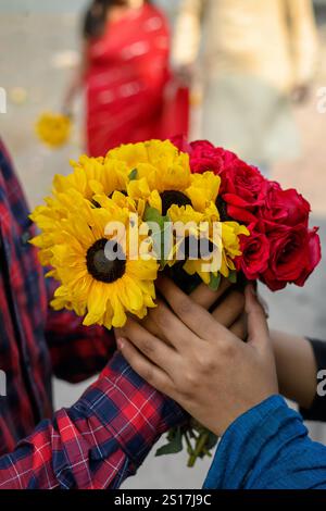 Close-up view of a couple holding a beautiful bouquet of sunflowers and roses against a blurred background, celebrating love. Stock Photo