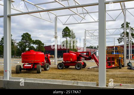 Modern red self propelled construction hydraulic articulating arm boom lifts platforms on modern metal frame building construction site Stock Photo