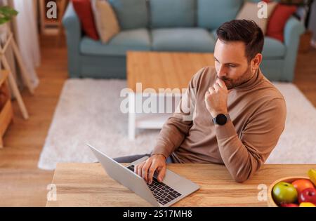 High angle view of focused businessman reading e-mails over laptop while working at desk in apartment Stock Photo