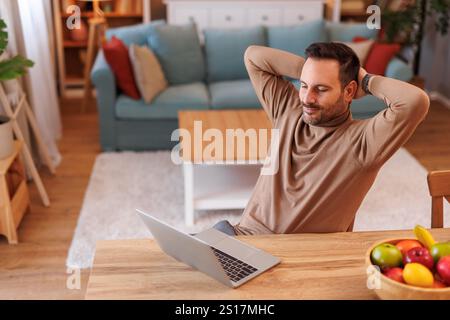 High angle view of tired mid adult man with hands behind head looking at laptop while resting at desk Stock Photo