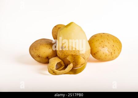 Raw potatoes, one of them half-peeled, exposing the interior of the tuber,white background.Solanum tuberosum. Stock Photo