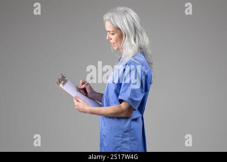 Middle aged woman doctor in scrubs writing notes on a clipboard Stock Photo
