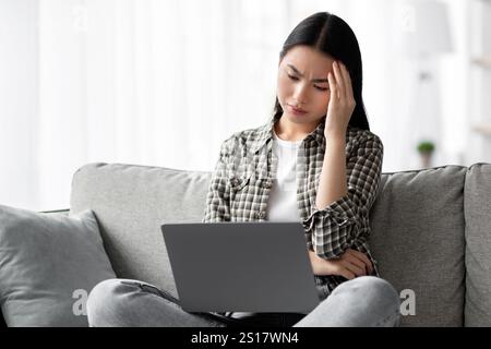 Exhausted korean lady suffering from headache while using laptop Stock Photo