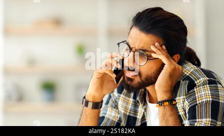 Upset middle-eastern guy having phone conversation, home interior Stock Photo