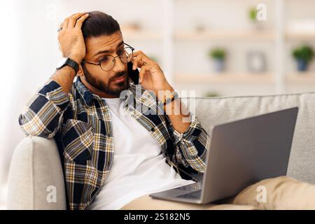 Stressful indian guy with laptop having phone conversation Stock Photo