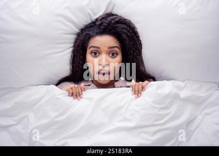 Surprised young woman in sleepwear waking up in cozy bedroom with natural daylight Stock Photo