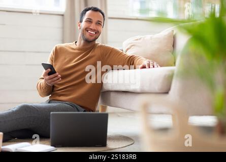 Young Arab man holding phone using pc at home Stock Photo