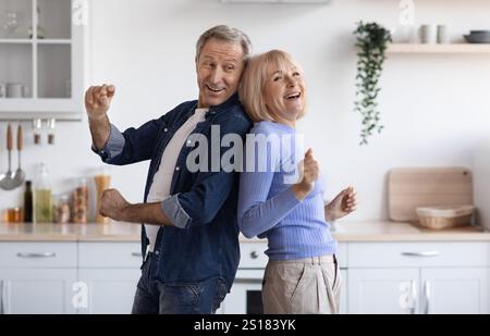 Joyful elderly spouses dancing together at kitchen Stock Photo