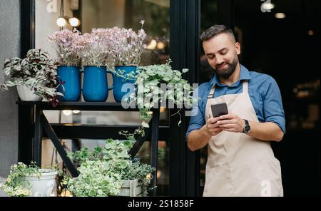 Portrait of young caucasian male owner of flower center typing on phone Stock Photo