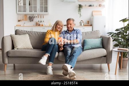 Happy Mature Husband And Wife Using Smartphone Sitting At Home Stock Photo