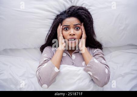 Young woman in pajamas looking surprised while waking up in bed with natural daylight Stock Photo