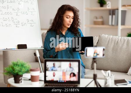 Lady teacher explaining math online showing tablet to laptop Stock Photo