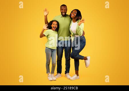 Family concept. Happy african american man, woman and girl waving hands to camera and smiling over yellow background Stock Photo