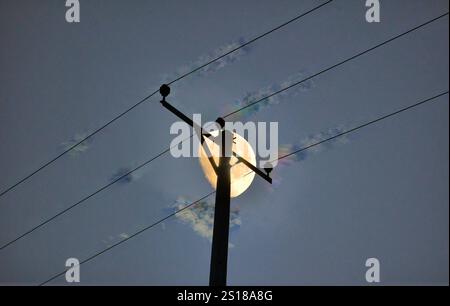 Telegraph power lines comms cables against illuminated half moon  and dark sky Stock Photo
