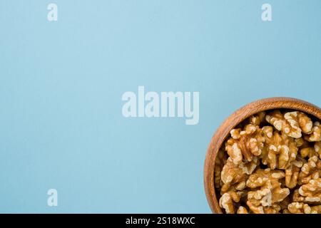 Top view of heap of walnut kernels in wooden bowl on blue background Stock Photo