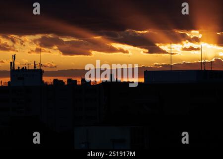 Orange sun rays stretch out from in between lines of dark clouds on the sky at dusk. Crows can be seen enjoying the orange hued horizon. Stock Photo