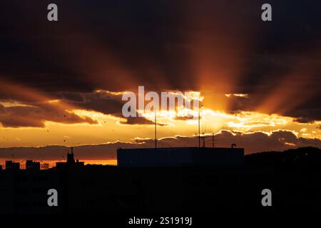 The setting sun sends streaks of light across the sky at dusk as it disappears behind clouds covering the horizon. Stock Photo
