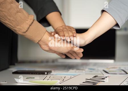 Collaborative Teamwork in UX UI Design Process with Hands Stacked Over Design Documents and Digital Devices Stock Photo