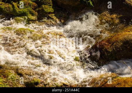 A close-up view of flowing water cascading over moss-covered rocks in a natural setting. Stock Photo