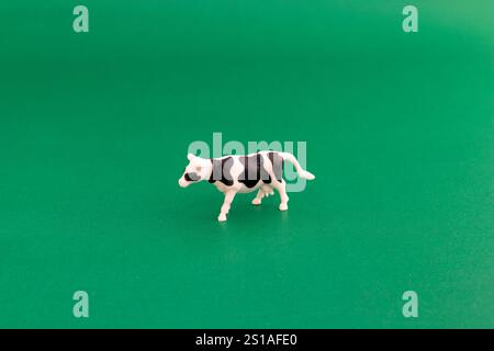 A single black and white plastic cow on green background Stock Photo