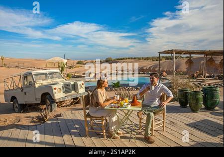 Morocco, Agafay, young couple having breakfast in front of the pool at the Anara camp in the agafay stone desert facing the Atlas mountains Stock Photo