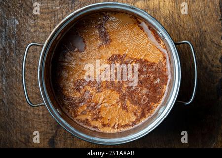 Freshly prepared cocoa drink in a metal pan on a wooden table, close up, top view Stock Photo