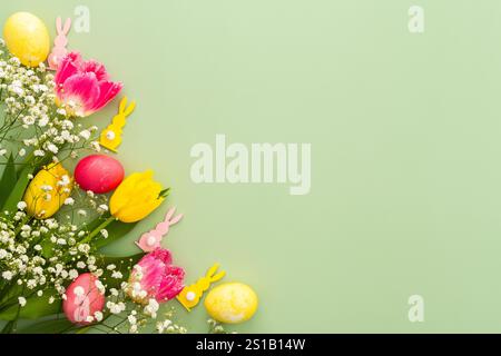 Spring Easter background, multi-colored Easter eggs with tulips and gypsophila and decorative bunnies on a green background Stock Photo