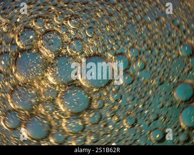 Golden bubbles intermingling in a blue liquid background create an abstract close-up artwork evoking serenity and curiosity. Perfect for creative back Stock Photo