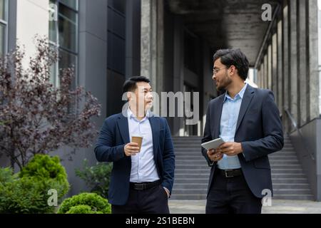 Two business colleagues walking down the street outside an office building, businessmen men in business attire talking and discussing, on a lunch break. Stock Photo