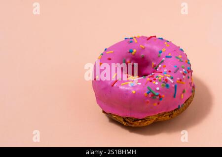 Donut with pink icing and colorful sprinkles on pink background Stock Photo