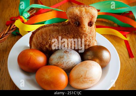 Small Easter lamb cake and painted eggs on a white plate and an Easter whip with colorful ribbons in the background Traditional Czech Easter symbols Stock Photo