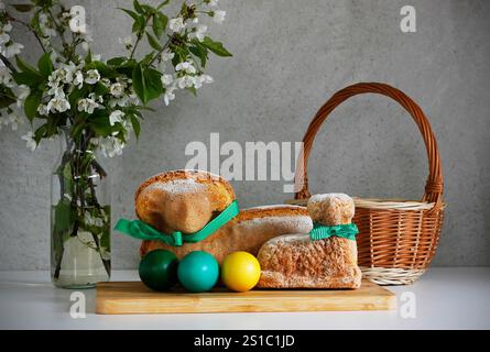 Easter still life containing two lamb cakes, three painted eggs, a wicker basket and blooming cherry twigs in a vase, gray background, copy space. Stock Photo