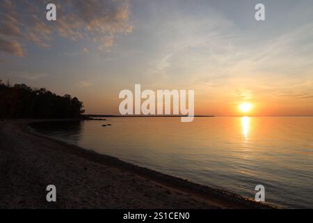 fiery ball of sun hovers above a lake throwing a brilliant streak across the water Stock Photo