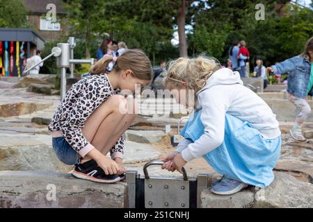 Two sisters, 8 and 7 play with a water feature in a playground at Brent Cross Town, a development in NW London Stock Photo