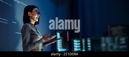 asian woman programmer standing in front of a screen with code projected  presentation the integration of technology and human expertise in software d Stock Photo