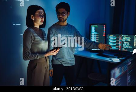 Asian Two software developers engaged in collaborative coding session, with code projected onto the wall and multiple computer screens displaying Stock Photo
