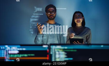 Asian Two software developers engaged in collaborative coding session, with code projected onto the wall and multiple computer screens displaying Stock Photo
