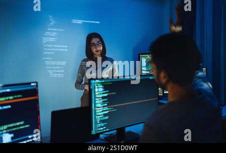 asian woman developers collaborating on a coding project, with one member presentation at code projected on the wall while the other works on multiple Stock Photo