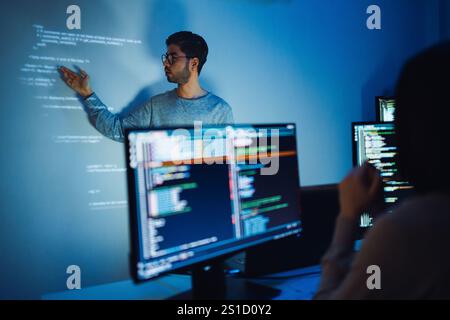 Indian man programmer standing in front of a screen with code projected  presentation the integration of technology and human expertise in software de Stock Photo