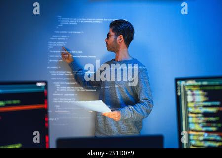 Indian man programmer standing in front of a screen with code projected  presentation the integration of technology and human expertise in software de Stock Photo