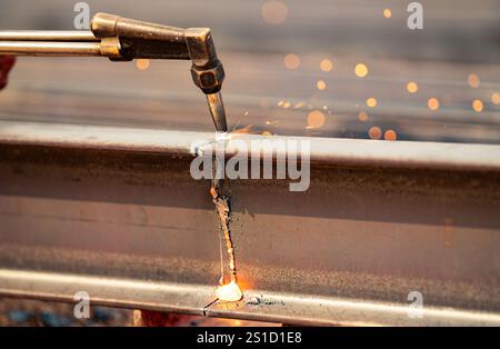 Welder using gas torch to cut metal beam, with sparks flying. Skilled craftsmanship and risks involved in industrial metal fabrication. Precision Stock Photo