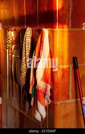 Sunlit scene with vibrant kitchen towels hanging on a warm ceramic tiled wall adding visual warmth. Stock Photo