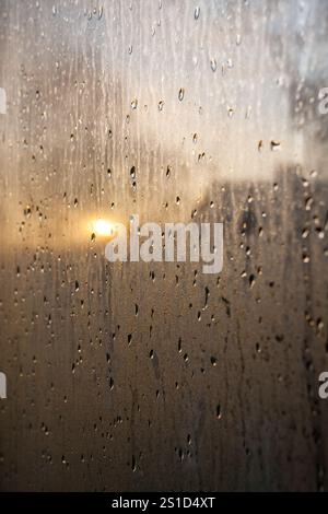 Close-up of water droplets on a window reflecting warm sunlight, creating an artistic and serene visual effect. Ideal for concepts like introspection, Stock Photo