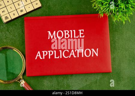 MOBILE APPLICATION words on the cover of a red notebook on a green saturated background. Stock Photo